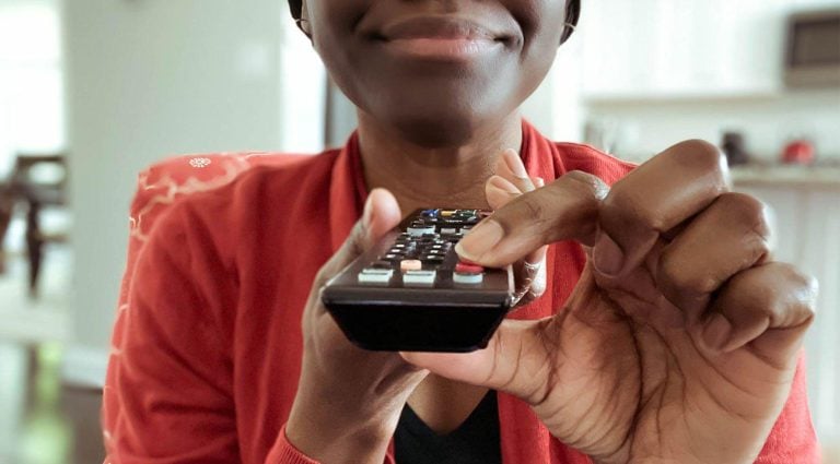 Woman holding TV remote pressing power button