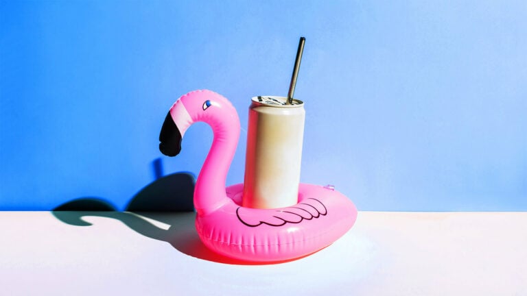 A soft drink can with a metal straw sitting in a small flamingo floatie